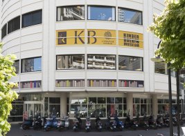 Image accompanying an article about reserving a workplace in the KB. Photo of the main entrance of the KB, with the logo of the KB and the Children's Book Museum on it.
