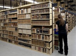 Collectiebehoud: een magazijn van de KB, met rijen boekenkasten en een medewerker die erlangs loopt. 