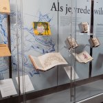 Een vitrine met boeken over oorlog en vrede en de tekst "Als je vrede wilt..." op de achtergrond.