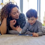 Vrouw en kind liggen op de grond en kijken samen naar een tablet.