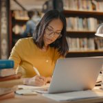 Vrouw doet onderzoek in bibliotheek achter laptop met boeken